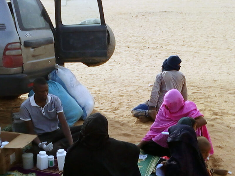 An International Medical Corps nurse dispenses medication after patients complete a medical consultation in the shade of the MMU.