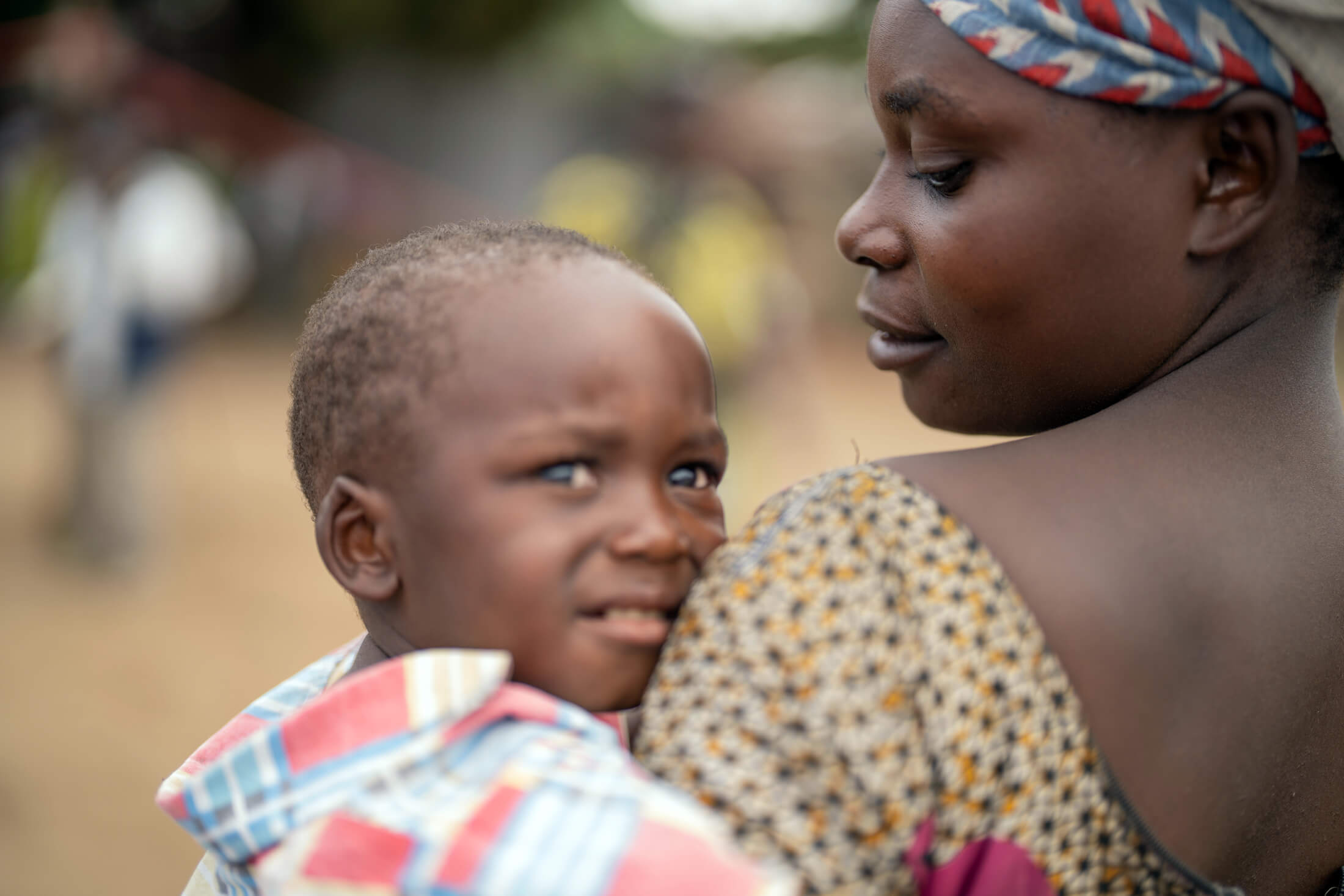 Georgette, who fled with her child from the conflict in the Masisi territory, stands holding her child outside the classroom that serves as her home.
