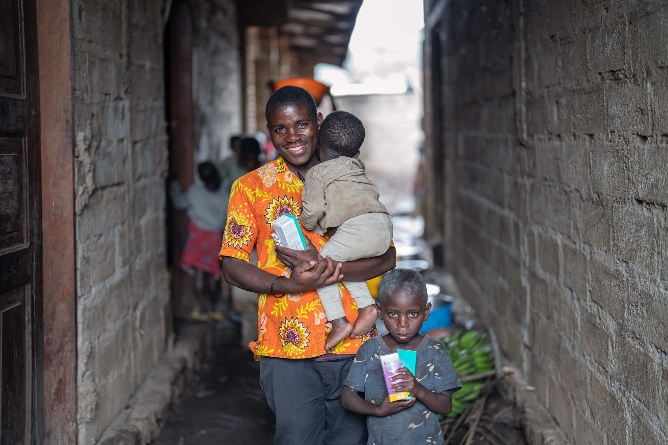 Uzima poses with his sons while holding the medications he received during his consultation with International Medical Corps MMU staff.