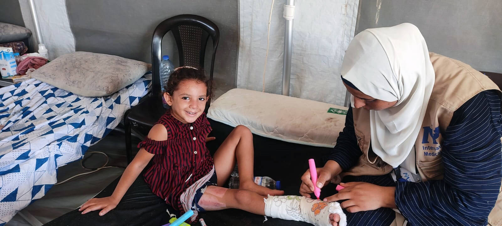 A staff member draws on Ghazal's cast in the hospital tent.