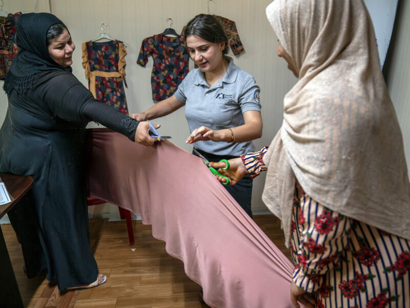 International Medical Corps Gender-Based Violence Manager Bahra Oshana (center) helps Fidha, 45 (left), and Mahsoma, 45 (right), cut fabric for their projects.