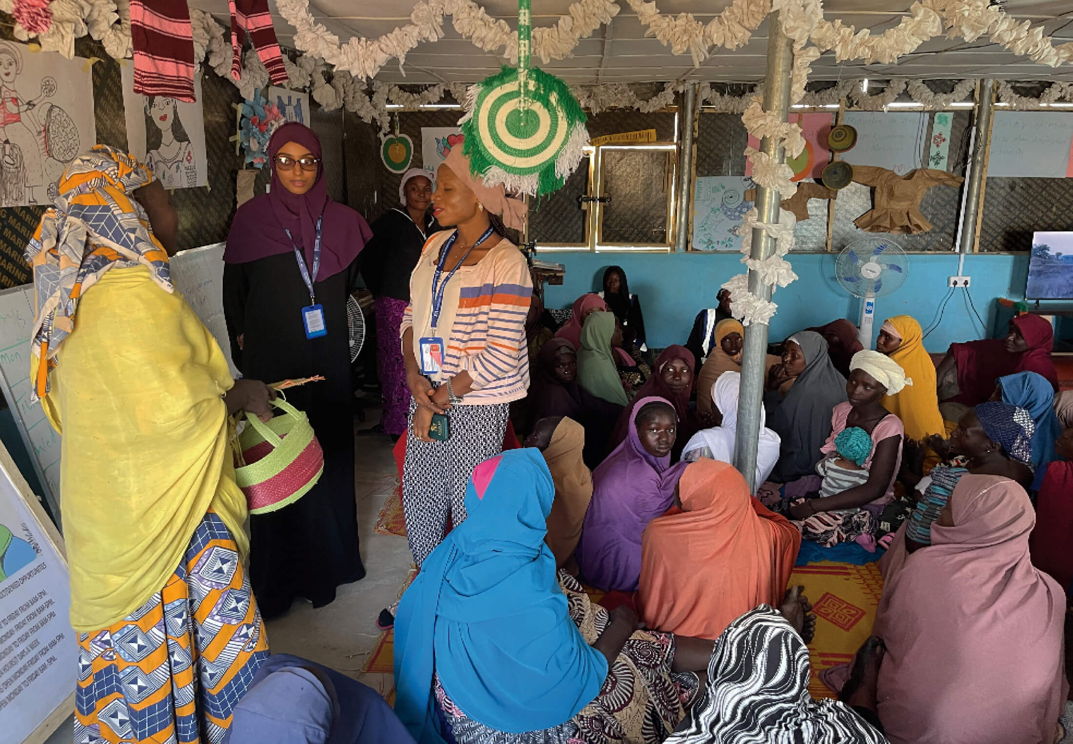 NIGERIA_Photo-2 Somalia GBV Coordinator Hiba Hassan Ahmed (in purple hijab) and Nigeria GBV Manager Sylvia Peter (in stripes) speak with women at the women’s and girls’ safe space in Pulka, Nigeria.
