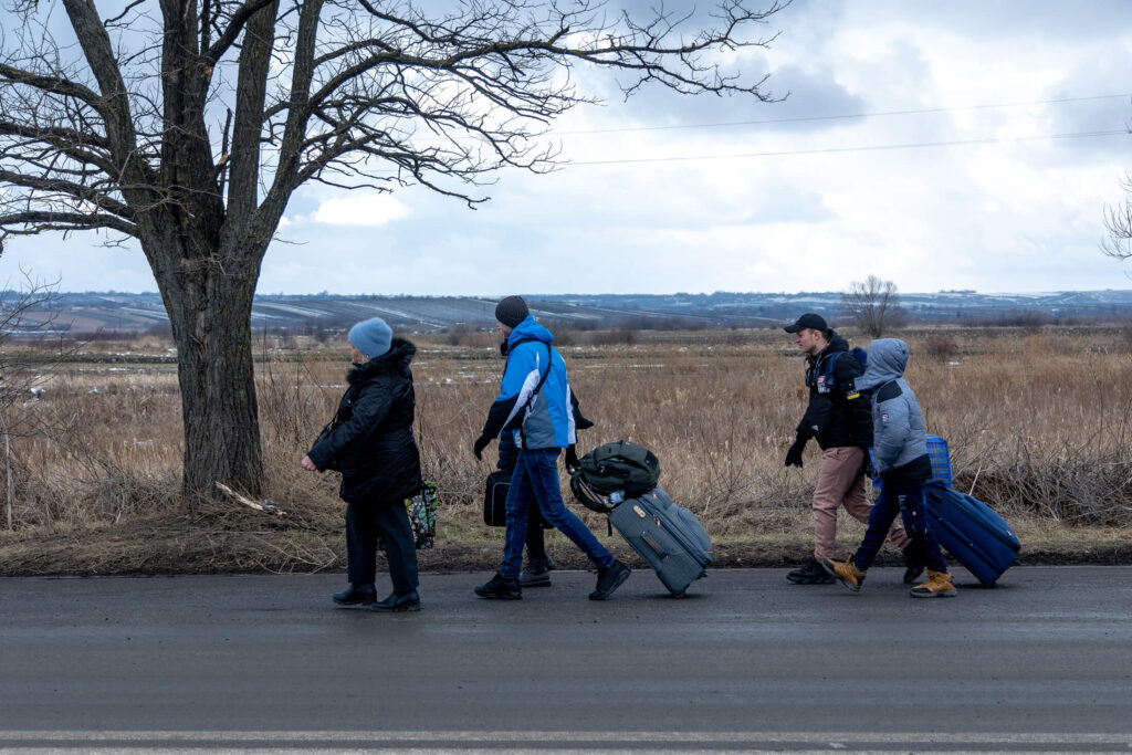 Ukrainian refugees walk along the road with their belongings.