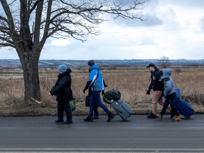 Ukrainian refugees walk along the road with their belongings.