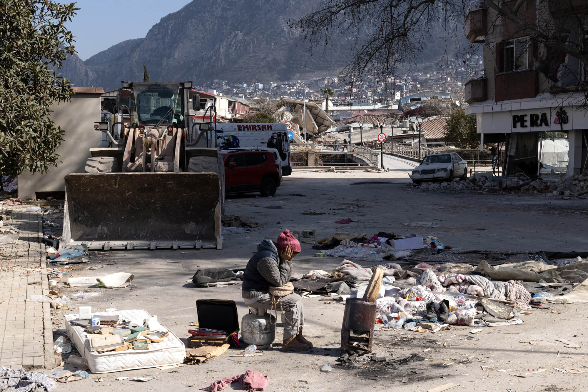 A young woman who survived the earthquakes sits next to rubble in Hatay, Türkiye.