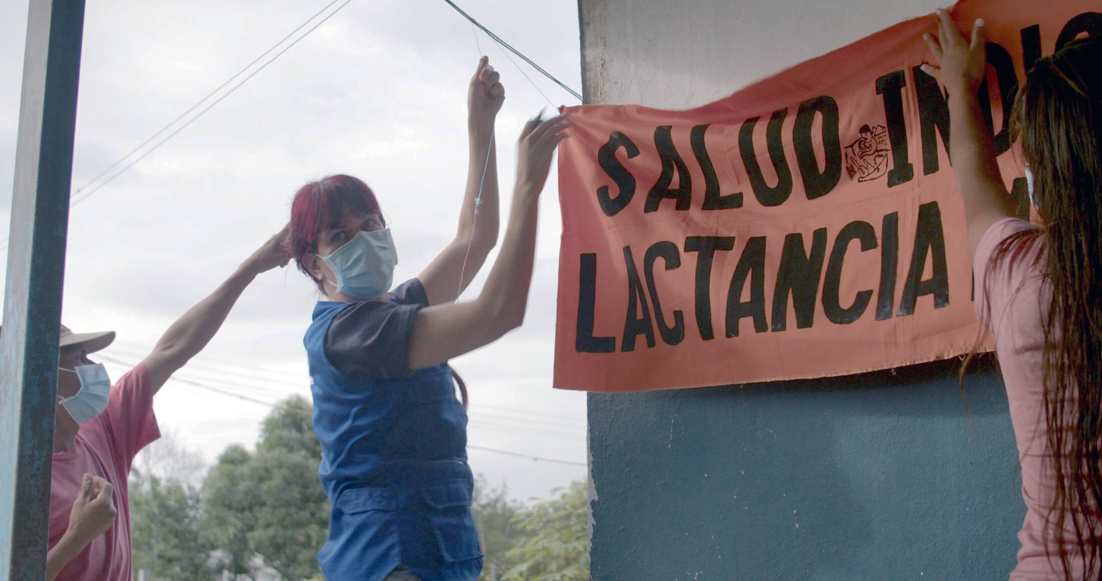 A Las Bombitas resident and a visiting healthcare professional raise a banner that tells locals they can receive breastfeeding nutrition and information at this location from International Medical Corps staff.