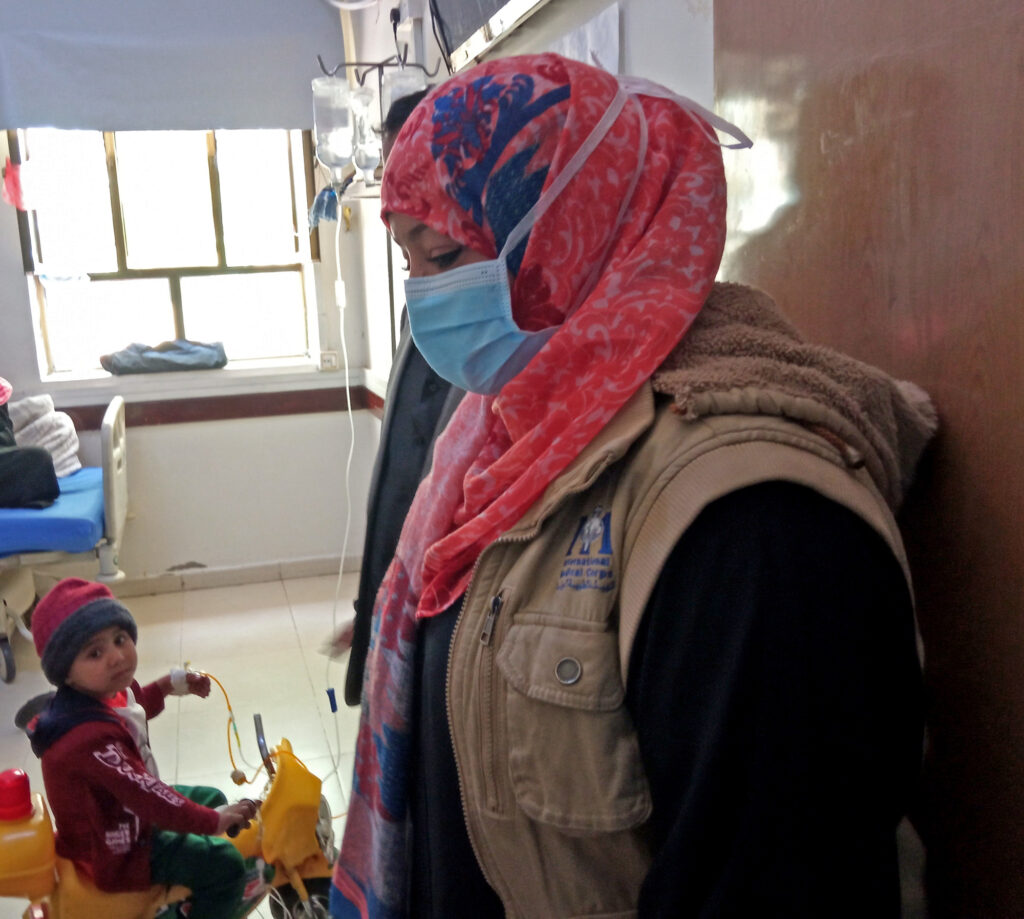 Our Health Program Manager in Sana’a, Nebras Khaled, on a visit to Yemen’s National Oncology Center in Sana’a. In the background is a young pediatric patient.